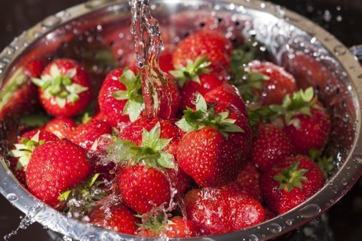 Red ripe strawberries in a stainless steel colander are rinsed under water