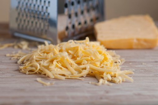 Grated cheddar cheese  with cheese grater and a block of cheese
