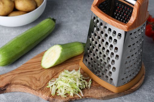 Grater and fresh zucchinis on grey table